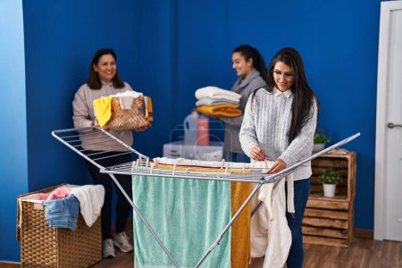 Photo for Three woman smiling confident hanging clothes on clothesline at laundry room - Royalty Free Image