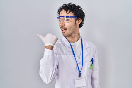 Photo for Hispanic man working at scientist laboratory pointing thumb up to the side smiling happy with open mouth - Royalty Free Image