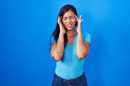 Téléchargez les photos : Jeune femme hispanique debout sur fond bleu avec la main sur la tête pour la douleur à la tête parce que le stress. migraine souffrant. - en image libre de droit