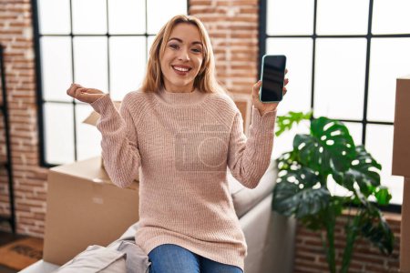 Téléchargez les photos : Femme hispanique se déplaçant vers une nouvelle maison montrant écran smartphone criant fier, célébrant la victoire et le succès très excité avec le bras levé - en image libre de droit