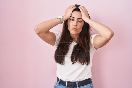 Téléchargez les photos : Jeune femme brune debout sur fond rose souffrant de maux de tête désespérés et stressés parce que la douleur et la migraine. mains sur la tête. - en image libre de droit