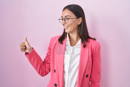 Téléchargez les photos : Jeune femme hispanique portant des vêtements de travail et des lunettes à la recherche fière, souriant faire les pouces vers le haut geste sur le côté - en image libre de droit