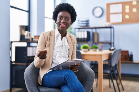 Téléchargez les photos : Jeune femme afro-américaine ouvrière d'entreprise écrivant sur la paperasse assis sur la chaise au bureau - en image libre de droit