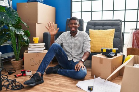 Téléchargez les photos : Afro-Américain assis sur le sol à la nouvelle maison montrant et pointant vers le haut avec les doigts numéro cinq tout en souriant confiant et heureux. - en image libre de droit