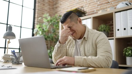 Téléchargez les photos : Jeune homme hispanique travailleur d'affaires stressé en utilisant un ordinateur portable au bureau - en image libre de droit