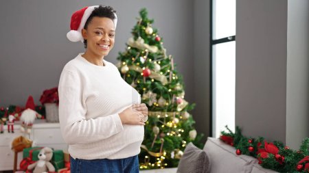Photo for Young pregnant woman touching belly celebrating christmas at home - Royalty Free Image
