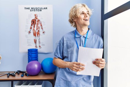 Photo for Young blond man pysiotherapist smiling confident reading document at rehab clinic - Royalty Free Image