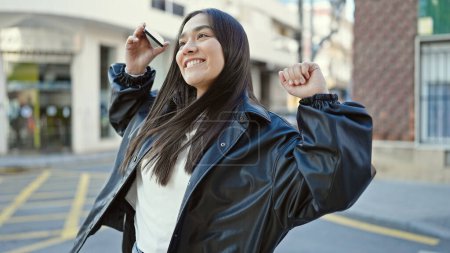 Téléchargez les photos : Jeune belle femme hispanique souriant confiant en utilisant smartphone dansant dans la rue - en image libre de droit