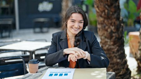 Téléchargez les photos : Jeune belle hispanique femme ouvrière regardant regarder sourire à la terrasse du café - en image libre de droit