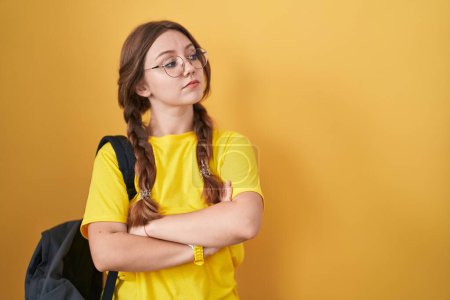 Photo for Young caucasian woman wearing student backpack over yellow background looking to the side with arms crossed convinced and confident - Royalty Free Image