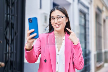 Téléchargez les photos : Chinois jeune femme faire appel vidéo avec smartphone souriant heureux pointant avec la main et le doigt - en image libre de droit