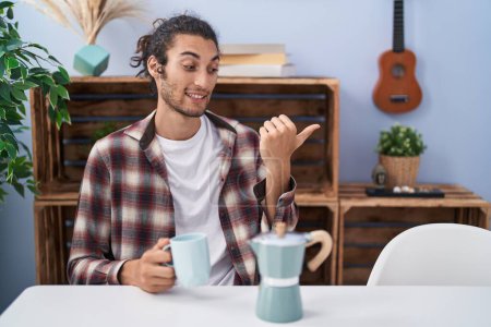 Téléchargez les photos : Jeune homme hispanique buvant du café de la cafetière française pointant le pouce vers le côté souriant heureux avec la bouche ouverte - en image libre de droit