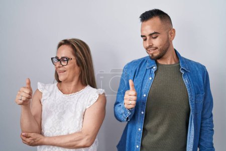 Foto de Madre e hijo hispanos de pie juntos luciendo orgullosos, sonriendo haciendo un gesto hacia un lado - Imagen libre de derechos