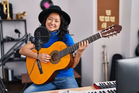 Photo for Young chinese woman artist singing song playing guitar at music studio - Royalty Free Image