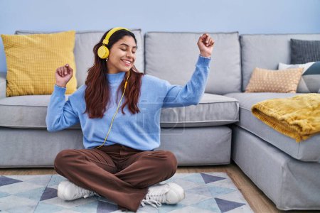Téléchargez les photos : Jeune femme hispanique écoutant de la musique assise sur le sol à la maison - en image libre de droit