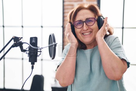 Foto de Senior mujer músico sonriendo confidente escuchar música en estudio de música - Imagen libre de derechos