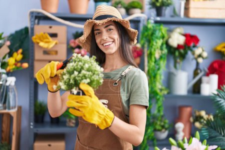 Photo for Young beautiful hispanic woman florist smiling confident cutting plant at flower shop - Royalty Free Image