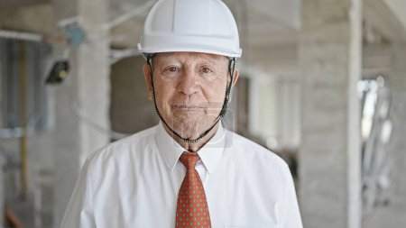 Foto de Arquitecto hombre de pelo gris senior de pie con expresión relajada en el sitio de construcción - Imagen libre de derechos
