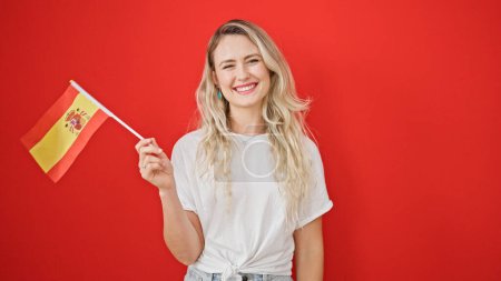 Photo for Young blonde woman smiling confident holding spanish flag over isolated red background - Royalty Free Image