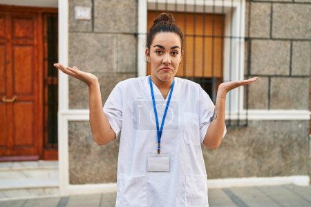 Foto de Mujer hispana joven con tarjeta de identificación del médico gritando y gritando fuerte a un lado con la mano en la boca. concepto de comunicación. - Imagen libre de derechos