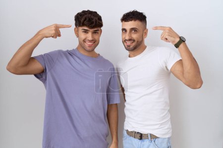 Téléchargez les photos : Couple gay homosexuel debout sur fond blanc souriant pointant vers la tête avec les deux mains doigt, grande idée ou pensée, bonne mémoire - en image libre de droit