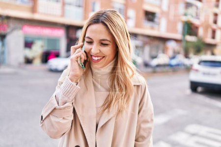 Téléchargez les photos : Jeune femme blonde souriant confiant parler sur smartphone à la rue - en image libre de droit