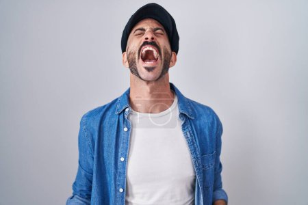 Foto de Hombre hispano con barba de pie sobre un fondo aislado enojado y loco gritando frustrado y furioso, gritando con ira. rabia y concepto agresivo. - Imagen libre de derechos