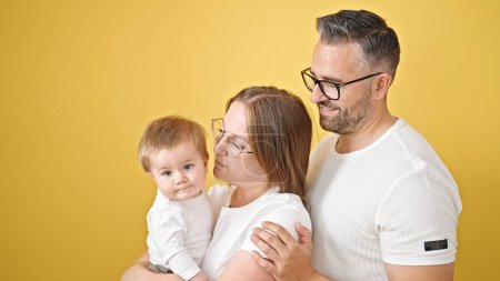 Téléchargez les photos : Famille de mère, père et bébé souriant ensemble sur fond jaune isolé - en image libre de droit