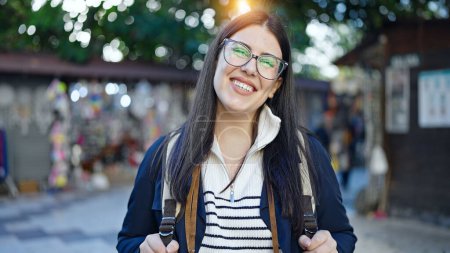 Photo for Young hispanic woman tourist wearing backpack smiling at street market - Royalty Free Image