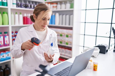Photo for Young blonde woman pharmacist scanning pills using laptop at pharmacy - Royalty Free Image