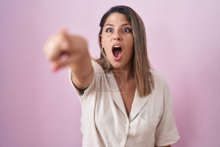 Photo for Blonde woman standing over pink background pointing with finger surprised ahead, open mouth amazed expression, something on the front - Royalty Free Image