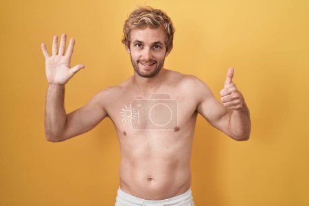 Téléchargez les photos : Homme caucasien debout torse nu portant écran solaire montrant et pointant vers le haut avec les doigts numéro six tout en souriant confiant et heureux. - en image libre de droit