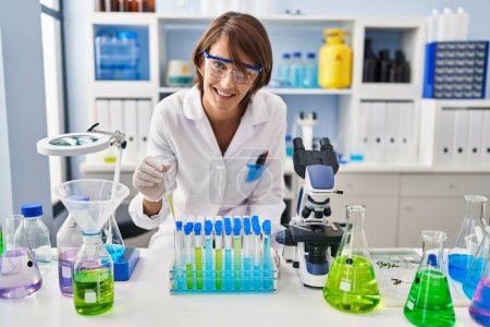 Photo for Young beautiful hispanic woman scientist pouring liquid on test tubes at laboratory - Royalty Free Image