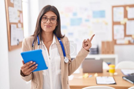Photo for Brunette young woman working at the office wearing stethoscope smiling happy pointing with hand and finger to the side - Royalty Free Image
