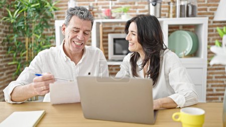 Photo for Senior man and woman couple using laptop reading document at dinning room - Royalty Free Image