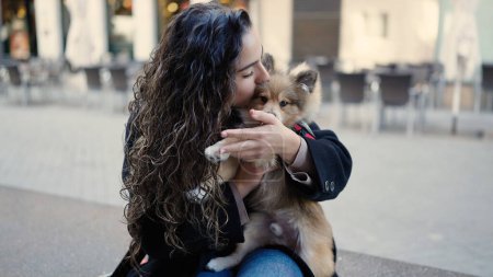 Téléchargez les photos : Jeune femme hispanique avec chien assis sur un banc embrassant dans la rue - en image libre de droit