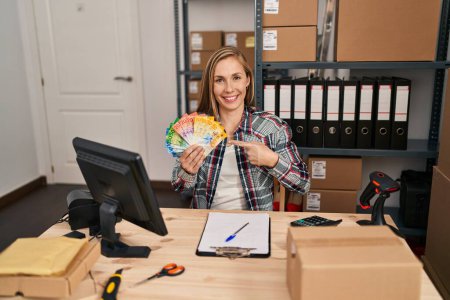Téléchargez les photos : Jeune femme blonde médecin travaillant dans une petite entreprise e-commerce tenant francs suisses souriant heureux pointant avec la main et le doigt - en image libre de droit