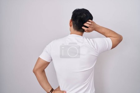Téléchargez les photos : Jeune homme asiatique debout sur fond blanc vers l'arrière pensant au doute avec la main sur la tête - en image libre de droit