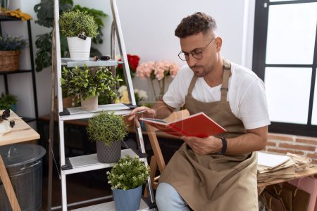 Photo for Young hispanic man florist reading notebook at flower shop - Royalty Free Image