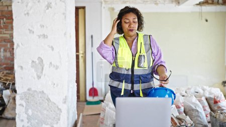 Téléchargez les photos : Jeune belle constructeur de femmes latines utilisant un ordinateur portable enlevant casque et lunettes sur le chantier de construction - en image libre de droit