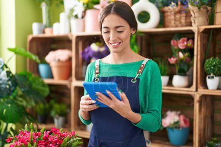 Photo for Young beautiful hispanic woman florist smiling confident using touchpad at flower shop - Royalty Free Image