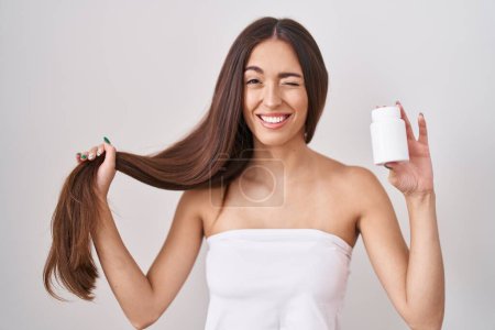 Téléchargez les photos : Jeune femme hispanique tenant les cheveux avec la main et les pilules clin d'oeil en regardant la caméra avec une expression sexy, visage joyeux et heureux. - en image libre de droit