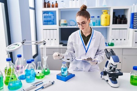 Téléchargez les photos : Jeune femme scientifique lisant un document mesurant un liquide au laboratoire - en image libre de droit