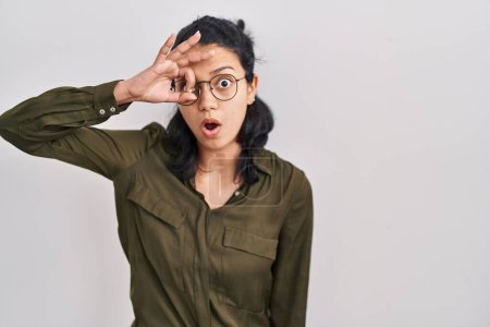 Photo for Hispanic woman with dark hair standing over isolated background doing ok gesture shocked with surprised face, eye looking through fingers. unbelieving expression. - Royalty Free Image