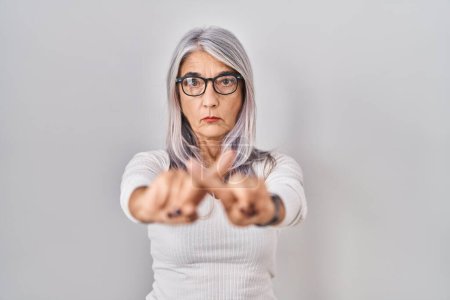 Foto de Mujer de mediana edad con el pelo gris de pie sobre fondo blanco rechazo expresión cruzando los dedos haciendo signo negativo - Imagen libre de derechos