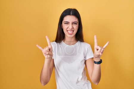 Photo for Young beautiful woman standing over yellow background shouting with crazy expression doing rock symbol with hands up. music star. heavy music concept. - Royalty Free Image