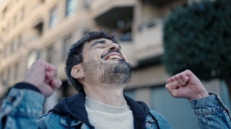 Téléchargez les photos : Jeune homme hispanique souriant confiance debout avec expression gagnante dans la rue - en image libre de droit