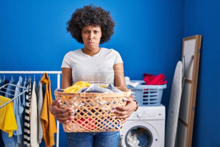 Foto de Black woman with curly hair holding laundry basket skeptic and nervous, frowning upset because of problem. negative person. - Imagen libre de derechos