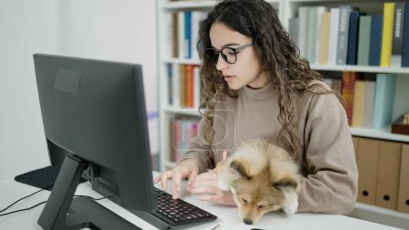 Photo for Young hispanic woman with dog student using computer studying at library university - Royalty Free Image