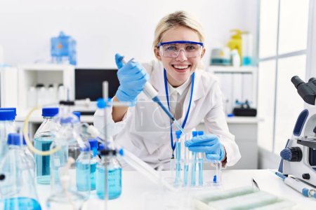Photo for Young blonde woman scientist pouring liquid on test tube at laboratory - Royalty Free Image